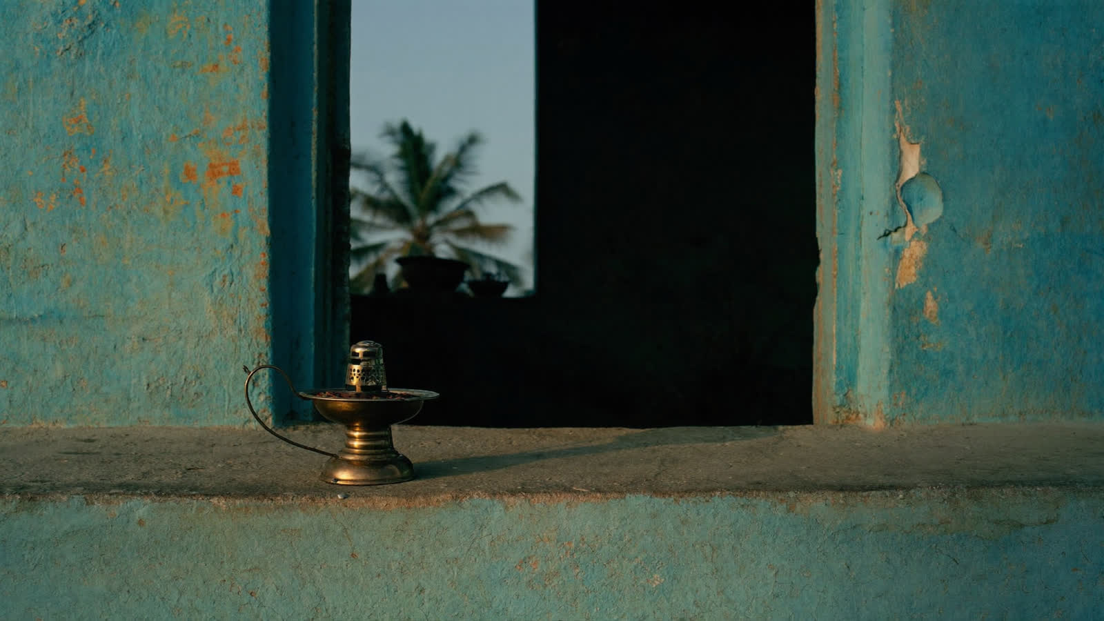 A brass oil lamp sitting unlit on the threshold of a village doorway before dawn.